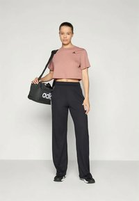 Ροζ cropped t-shirt, μαύρα αθλητικά παντελόνια με λευκές πλαϊνές ρίγες και μια μαύρη τσάντα με λευκό λογότυπο, φορεμένος από μοντέλο που στέκεται όρθιο.