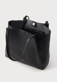 Czarna skórzana torba na ramię o teksturowanym wykończeniu, z otwartą górą i pojedynczym paskiem na ramię. Zawiera wewnętrzną kieszeń na zamek i zapięcie magnetyczne.