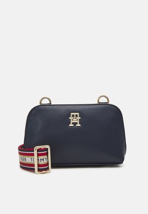 Sac à main en cuir marine avec un logo doré, fermeture zippée et double poignées supérieures. Inclus une sangle ajustable à rayures multicolores pour plus de polyvalence.