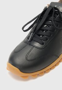 Sneaker in pelle nera con suola in gomma, cuciture a texture, punta rotonda e lacci neri. Branding discreto sulla linguetta.