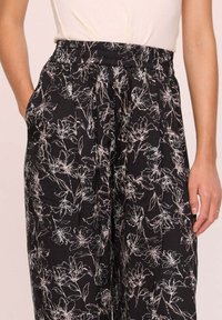 Pantalons noirs à fleurs avec des fleurs dessinées aux lignes blanches, ceinture élastique et poches latérales. Tissu léger avec une coupe décontractée.
