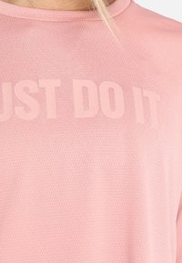 Camiseta deportiva rosa con una tela texturizada y la frase "SIMPLEMENTE HAZLO" impresa de manera prominente en un tono más claro en la parte frontal.