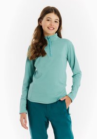 Dlhý rukáv, zipsový top v modro-zelenom materiáli, s polo golierom a hladkou textúrou. Spárované s modro-zelenými nohavicami a umiestnené na bielom pozadí.