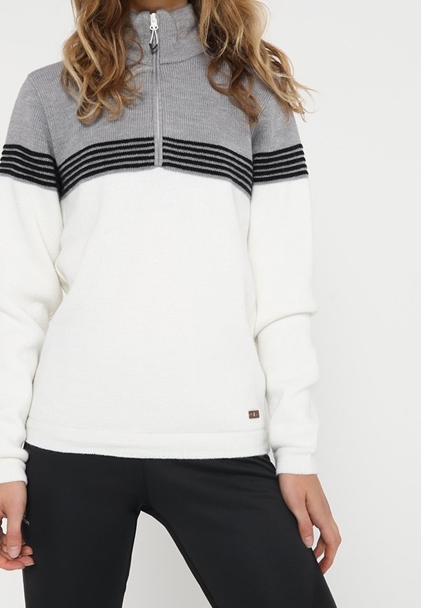 Femme portant un pull à manches longues avec un haut gris, des rayures horizontales noires et un bas blanc, associé à un pantalon noir.