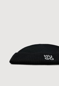 Berretto a coste nero con bordo ripiegato e piccolo logo "MUGO" bianco decorato su sfondo bianco.