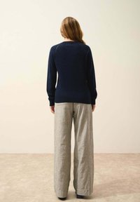 Pull marin à manches longues, avec des poignets côtelés et une silhouette ajustée, associé à un pantalon en lin gris à jambes larges avec une texture subtile.