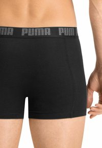 Black boxer briefs made from a smooth, stretchy fabric. Features a wide elastic waistband with "PUMA" logo in gray. Neat stitching on seams.
