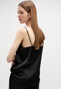 Svart sateng cami med tynne justerbare stropper, med blonde detaljer langs ryggen, glatt tekstur og draperende passform.