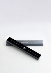 Svart smyckesask med "Sofia Milani Jewels" logotyp, som innehåller ett delikat silverarmband med en cirkulär berlock med tassavtrycksdesign.