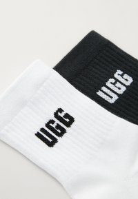 Sorte og hvide sokker lavet af en bomuldsblanding, med ribbet tekstur og dristig "UGG" branding i kontrasterende farver på hver sok.