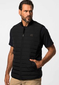 Schwarze Pufferweste mit einem Reißverschluss, ausgestattet mit horizontalen Steppnähten, seitlichen Taschen und einem hohen Kragen. Schlichte Logodetails vorne.