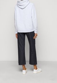 Felpa grigia chiaro con cappuccio regolabile e orlo a costine, abbinata a pantaloni wide-leg in denim scuro e sneakers bianche.