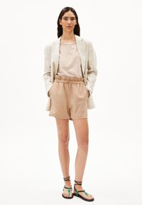 Beige linnen blazer over een gestreept licht topje, gecombineerd met tan elastische taille shorts en zwarte sandalen met groene accenten.