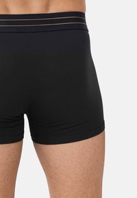 Czarne bokserki o dopasowanym kroju, wykonane z miękkiego materiału, z gładkim pasem w talii ozdobionym trzema poziomymi złotymi paskami.