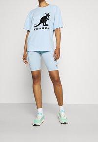 Camiseta de gran tamaño en azul claro con logo negro de Kangol, combinada con pantalones cortos de ciclismo en azul claro. El calzado presenta acentos en blanco y verde menta.