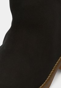 Bottines en velours noir avec une texture lisse et des détails de couture le long de la semelle. Le design présente un bout rond et un petit talon plat.