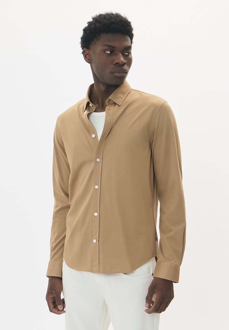 Svetlohnedá košeľa s dlhým rukávom vyrobená z hladkej tkaniny, s zapínaním na gombíky, špicatým golierom a bielymi gombíkmi.