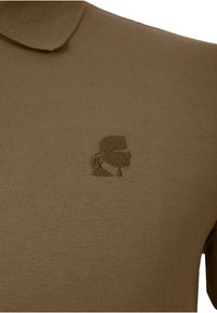 Polo marrón hecho de una tela suave, con un logotipo bordado discreto en forma de perfil en el lado izquierdo del pecho.