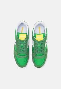Baskets vertes en tissu et daim, avec un panneau latéral blanc, des lacets verts et un logo jaune sur la languette.