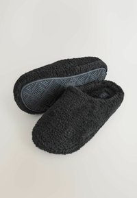 Papuci negri din material plușat, cu un exterior texturat și pufos, și o talpă din cauciuc cu un model geometric pe bază pentru aderență și durabilitate.