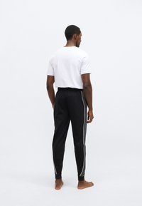 Čierne tepláky so sivým bočným panelom a bielym lemovaním, doplnené o jednoduché biele tričko s krátkym rukávom, zobrazené zozadu.