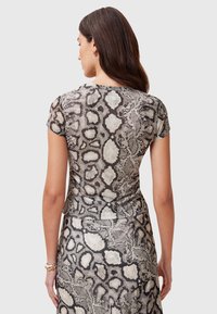 Top a maniche corte in tessuto leggero e trasparente, caratterizzato da un motivo a stampa serpente in bianco e nero e design aderente, con scollo rotondo.