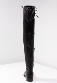 Bota negra de cuero texturizado alta con tacón bajo, cremallera trasera y cordones en la parte superior, sobre un fondo blanco.