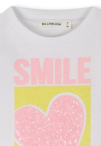 Weißes T-Shirt mit pinkem "SMILE"-Schriftzug und einem großen pinken, glitzernden Herz auf gelbem Hintergrund. Weicher Stoff mit Rundhalsausschnitt.
