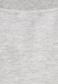 Hellgrauer Strickstoff, der eine subtile Textur mit einem gerippten Muster entlang der oberen Kante aufweist. Weiches, atmungsaktives Material.