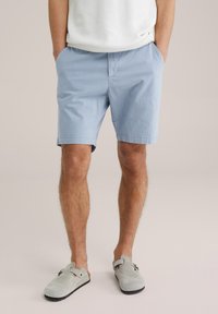Himmelblaue, gestreifte Shorts aus leichtem Stoff mit einem elastischen Bund und Seitentaschen. Kombiniert mit grauen Wildleder-Slipschuhen.