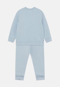 Completo da tuta azzurro chiaro composto da una maglietta con scollo rotondo e pantaloni con vita elasticizzata. Il tessuto ha una texture liscia con polsini e orlo a coste.