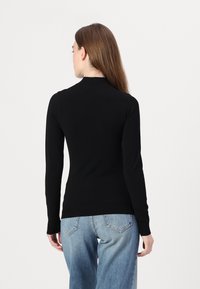 Svart langermet topp med høy krage, tettsittende design og glatt tekstur, kombinert med lyseblå denimjeans.