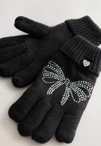 Black knitted gloves with ribbed cuffs, featuring a rhinestone bow design on one hand and a small heart-shaped button accent.