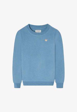 Niño con sudadera azul, pantalones cargo beige, deportivas azul marino y una gorra de béisbol amarilla y gris, de pie y mirando hacia un lado.