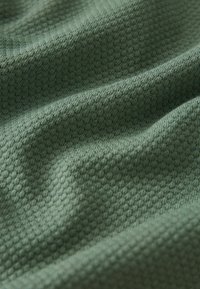 Textureret stof i mørkegrøn, med et subtilt honningkage mønster. Materialet ser blødt ud med synlige folder og dybde.