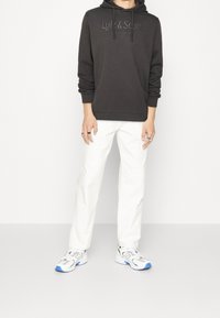 Felpa con cappuccio grigio scuro con logo Lyle & Scott, abbinata a pantaloni bianchi a gamba dritta e sneakers bianche con dettagli blu.