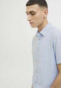 Camisa de botón de manga corta azul claro, hecha de una tela texturizada, con un cuello suave, botones en el frente y un corte relajado.