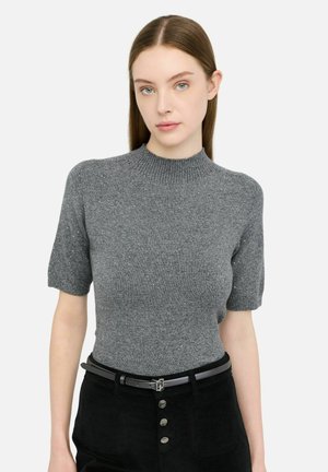 Suéter de punto gris de manga corta con cuello alto, con sutiles detalles brillantes y silueta ajustada. Se lleva con un cinturón negro.