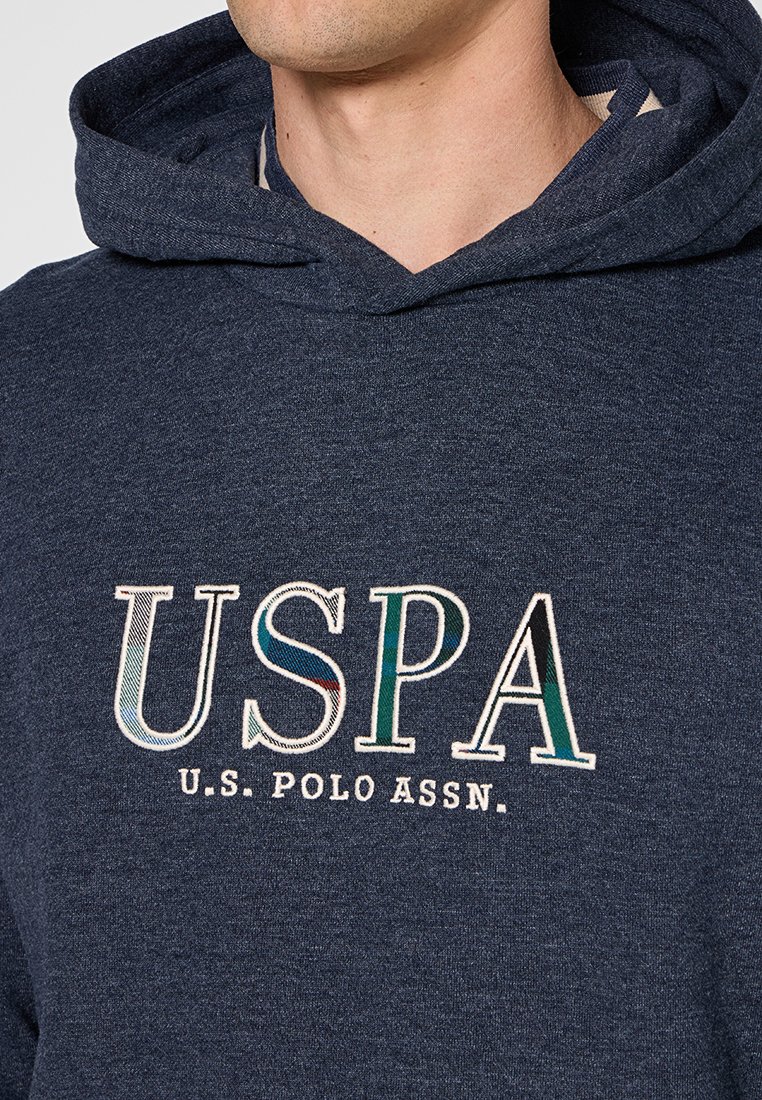 Homme portant un sweat à capuche bleu foncé avec les lettres multicolores "USPA" en grand et le texte "U.S. Polo Assn." brodé sur la poitrine.