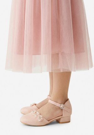 Bambina che indossa scarpe rosa glitterate con tacco basso, decorazioni floreali e cinturini alla caviglia, abbinate a una gonna di tulle rosa a più strati.