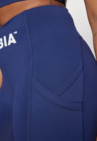 Tumši zila legingi ar gludu tekstūru, ar izliekta dizaina kabatu un kontrastējošām tumšām šuvēm. "Columbia" logo izdrukāts baltā krāsā.