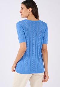 Suéter de punto azul claro con mangas cortas, que presenta un patrón de diamantes texturizado y un dobladillo acanalado, fabricado con un tejido suave y transpirable.