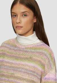 Pastel gestreepte gebreide trui met een zachte textuur, in tinten roze, lavendel en groen. Ronde halslijn gedragen over een witte turtleneck.