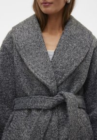 Manteau en laine texturée gris avec un large col, une taille ceinturée et un tissu doux et bouclé. Présente une coupe décontractée et un léger éclat.
