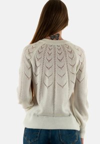 Pull en tricot blanc avec un motif de feuilles texturé dans le dos, des poignets ajustés et un col rond, associé à un jean en denim bleu.