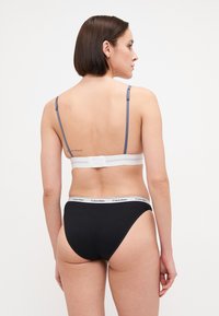 Svarte bomullsunderdeler med en hvit Calvin Klein midje, sammen med en hvit og blå bralette med justerbare stropper og krokfestesystem.