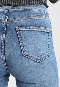 Jeans de mezclilla azul claro con diseño ajustado, que cuentan con bolsillos traseros con contornos cosidos y una textura ligeramente lavada.
