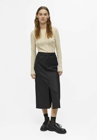 Cream ribbed long-sleeve top paired with a high-waisted black faux leather skirt featuring a front slit. Black lace-up shoes complete the look.