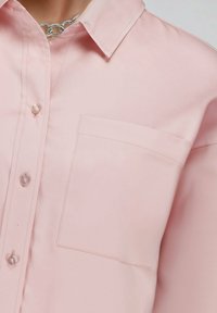 Lichtroze overhemd met knopen, gemaakt van soepel materiaal, met een borstzak, klassieke kraag en ronde knopen.