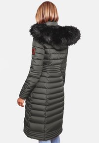 Padded long coat in dark green with a black fur hood trim, featuring a fitted waist and quilted pattern. Brown logo patch on the arm.